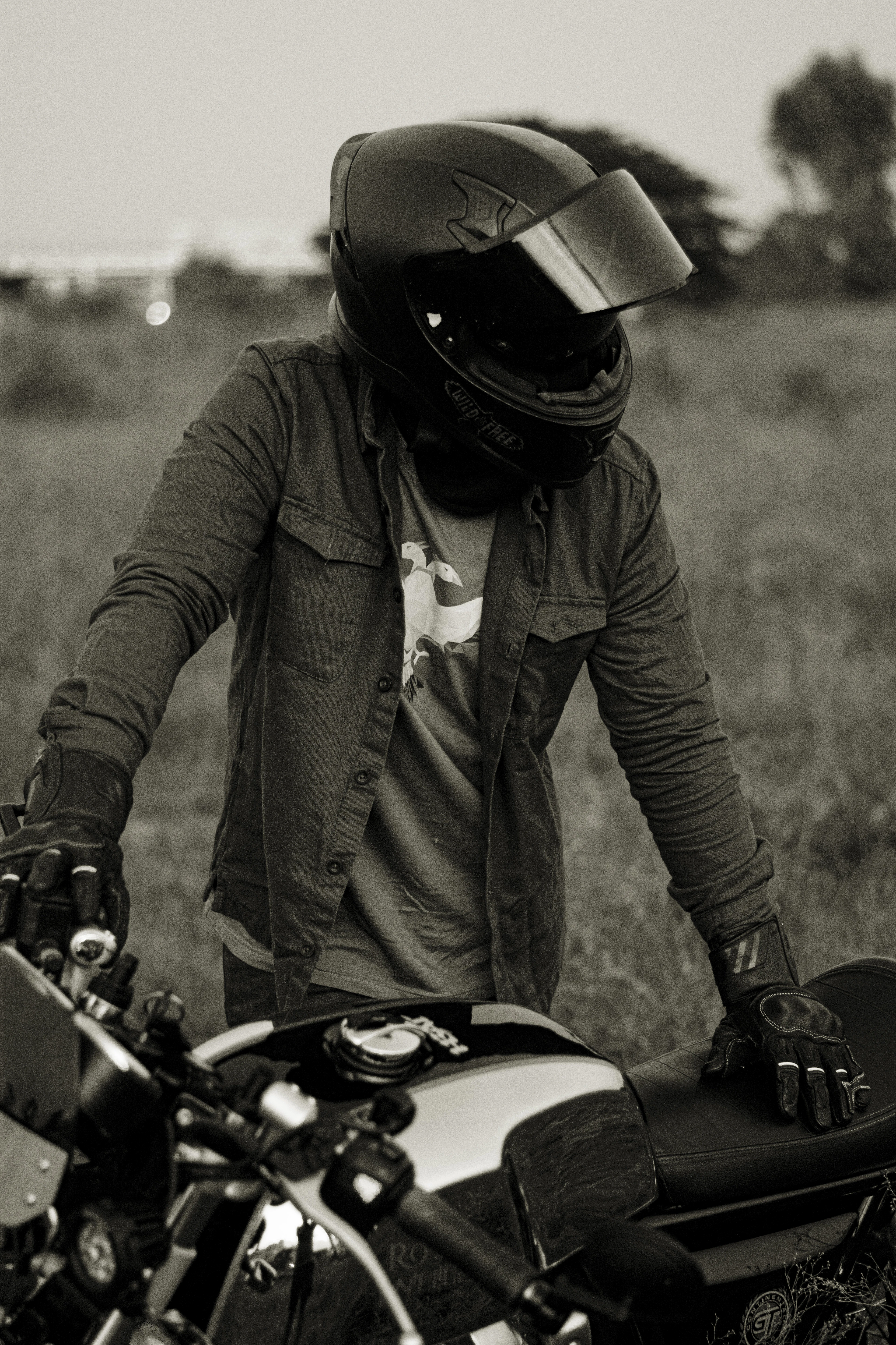 Black and white photo of a rider in a canvas jacket and modular helmet beside a motorcycle