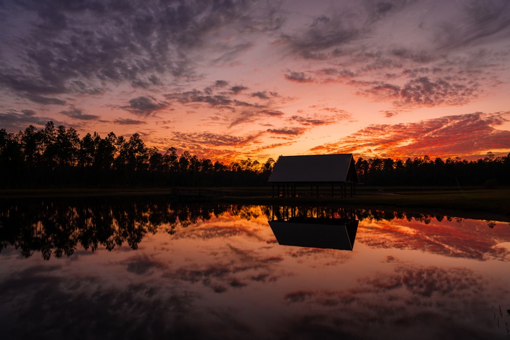 a barn sits in the middle of a lake as the sun sets