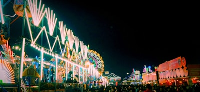 Crowd dancing joyfully under colorful carnival lights at night.