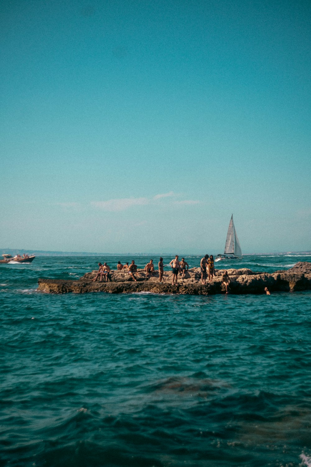 a group of people standing on a rock in the ocean