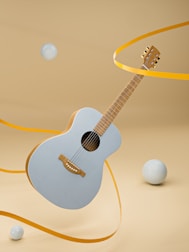 A light blue acoustic guitar is suspended in mid-air against a beige background. Yellow ribbons are winding around the guitar, and several light blue spheres are floating around it.