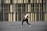 A person is dancing energetically in an open area with a modern building as the backdrop. The individual is wearing a white shirt, black pants, and white sneakers. Long red braids flow with the movement, conveying motion and style.