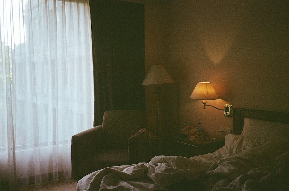 a bedroom with a bed, chair, lamp and window