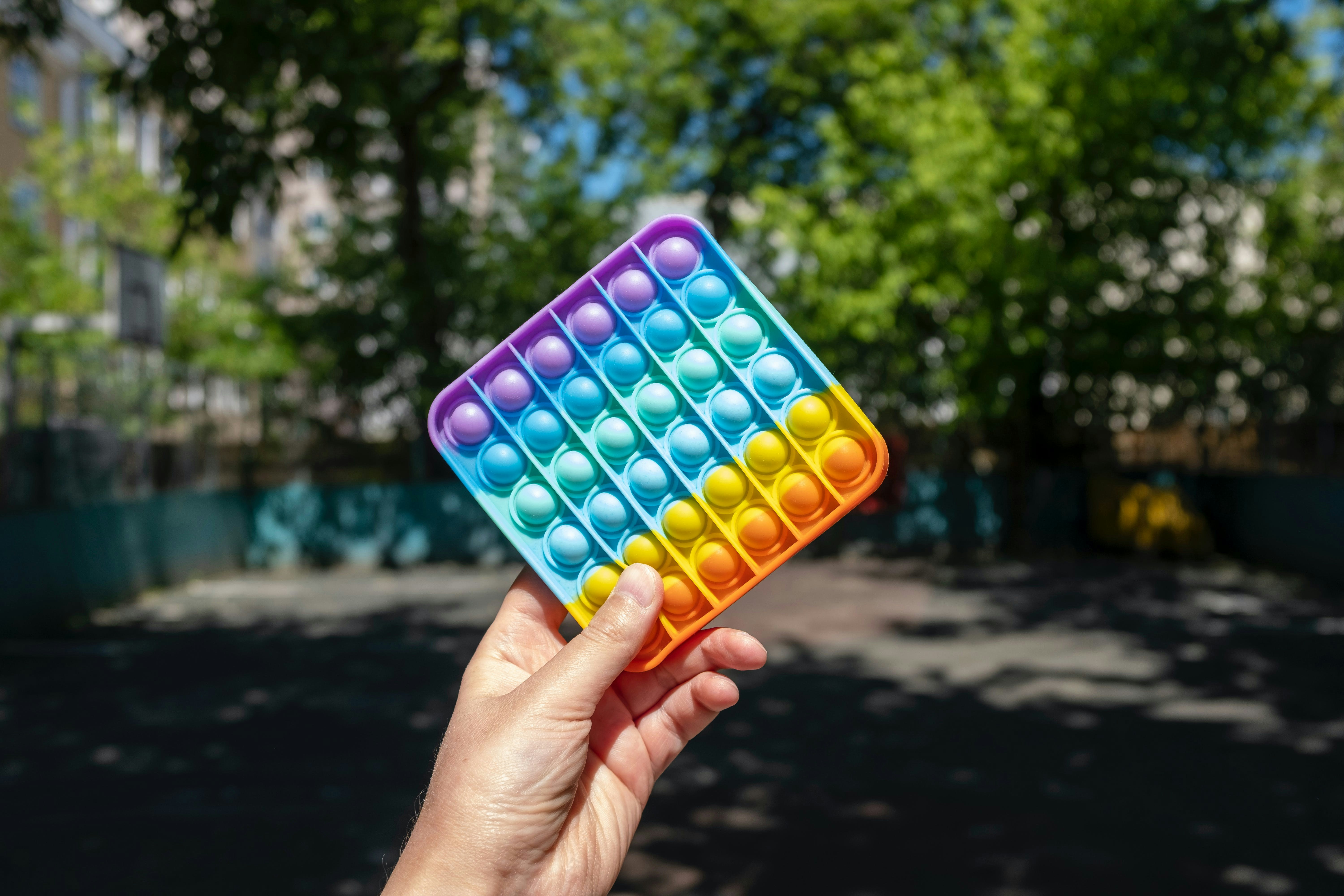 eine Hand, die ein buntes Spielzeug vor einem Baum hält