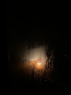 A dimly lit, rain-soaked window with a single letter resting on the sill, shadows hinting at a story of love and loss.