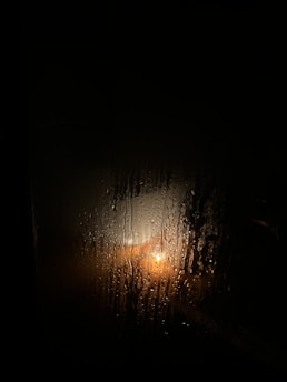 A dimly lit, rain-soaked window with a single letter resting on the sill, shadows hinting at a story of love and loss.