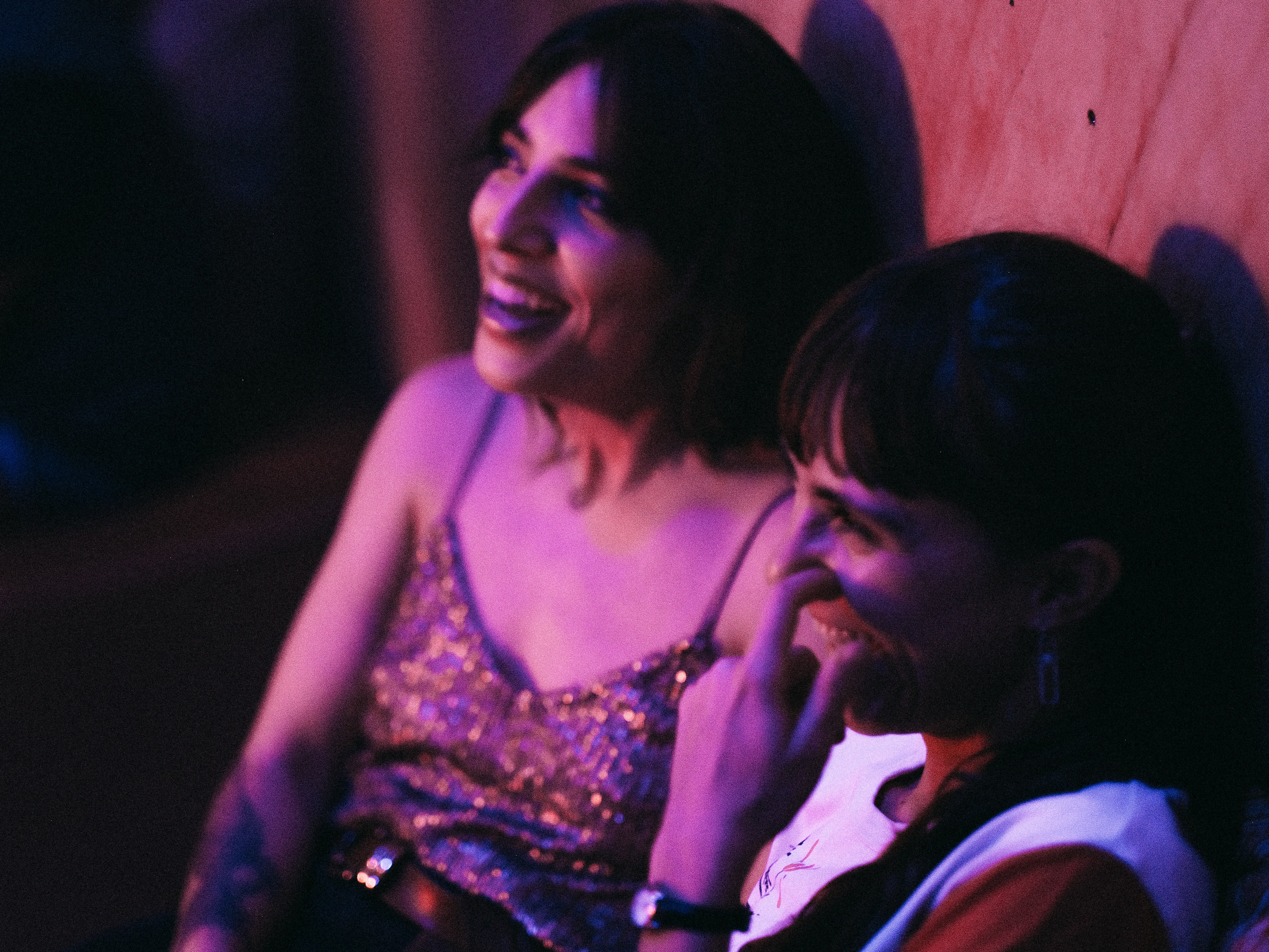 a couple of women sitting next to each other, people dancing in a night club