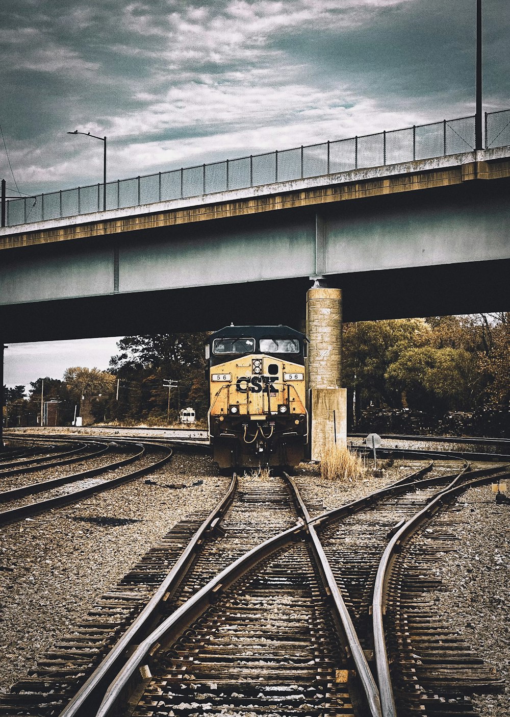 a yellow train traveling down train tracks under a bridge