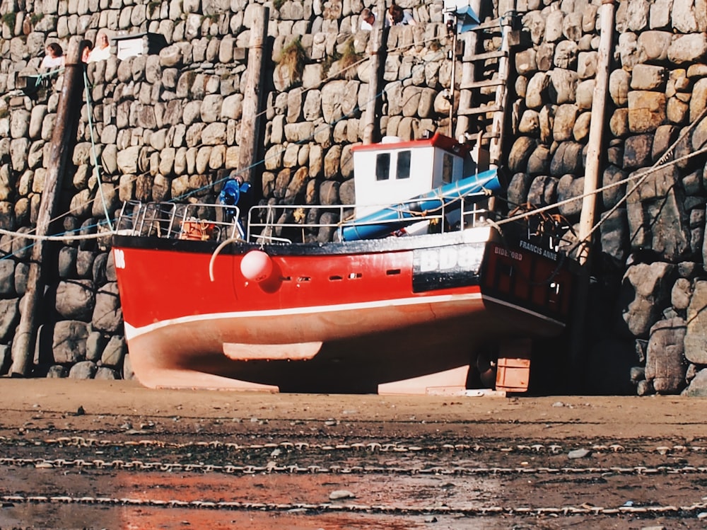 a red and white boat sitting next to a stone wall