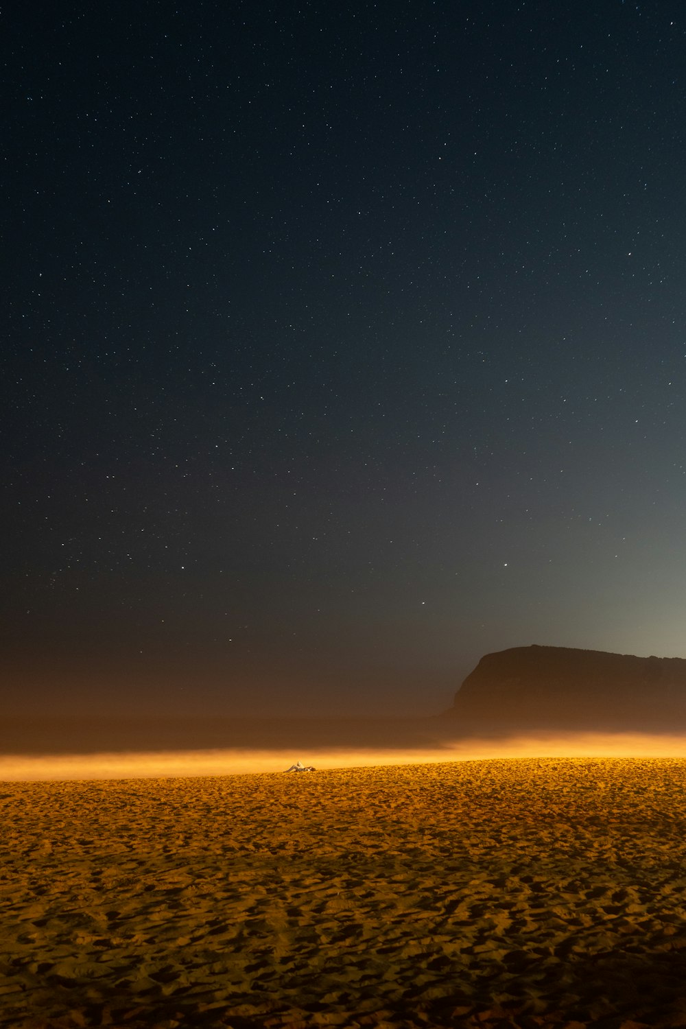 the night sky over a desert with a mountain in the distance