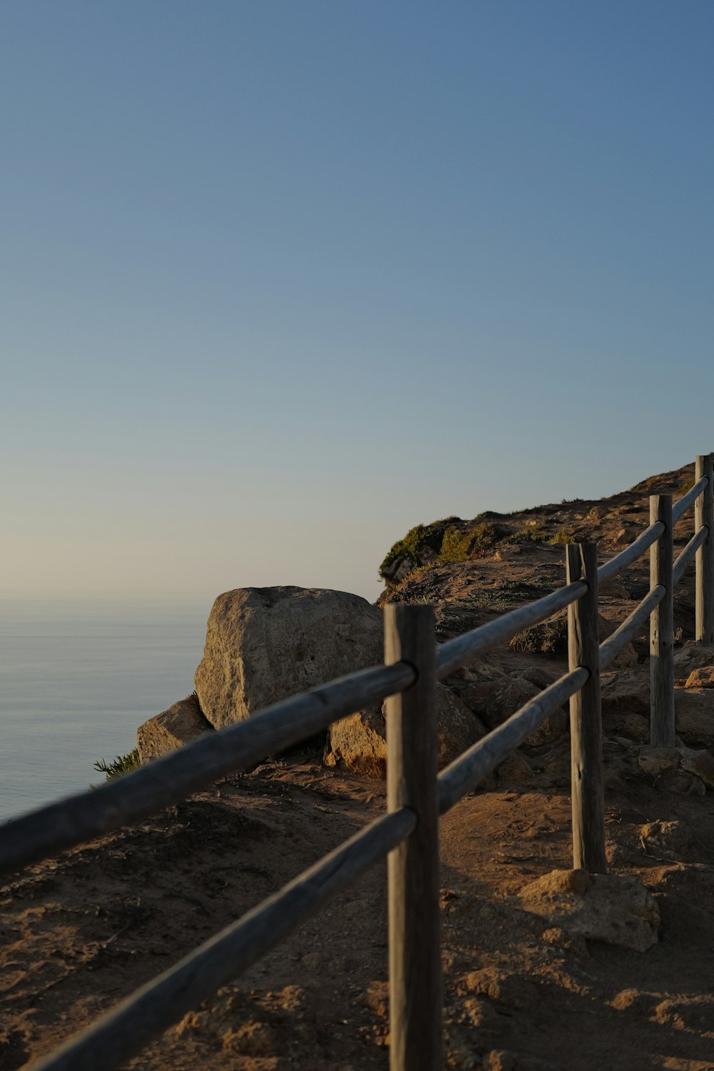 a wooden fence on top of a hill next to the ocean