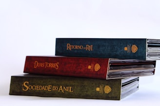 Three horizontally stacked DVD cases with the titles printed in gold letters on their spines. The cases are colored green, red, and dark blue, with the titles being 'A SOCIEDADE DO ANEL,' 'DUAS TORRES,' and 'RETORNO DO REI.'