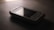 A vintage Samsung mobile phone with physical buttons is placed on a smooth, dark surface. The lighting is dim, creating a nostalgic and subdued atmosphere, casting soft shadows around the device.