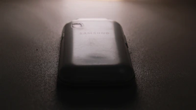 A close-up of a Samsung smartphone glowing on a wooden desk.