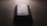A slightly worn smartphone with a visible Samsung logo on the back, placed on a flat, dark surface under low lighting conditions. The light source is coming from the top, casting subtle shadows around the phone.