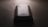 A slightly worn smartphone with a visible Samsung logo on the back, placed on a flat, dark surface under low lighting conditions. The light source is coming from the top, casting subtle shadows around the phone.