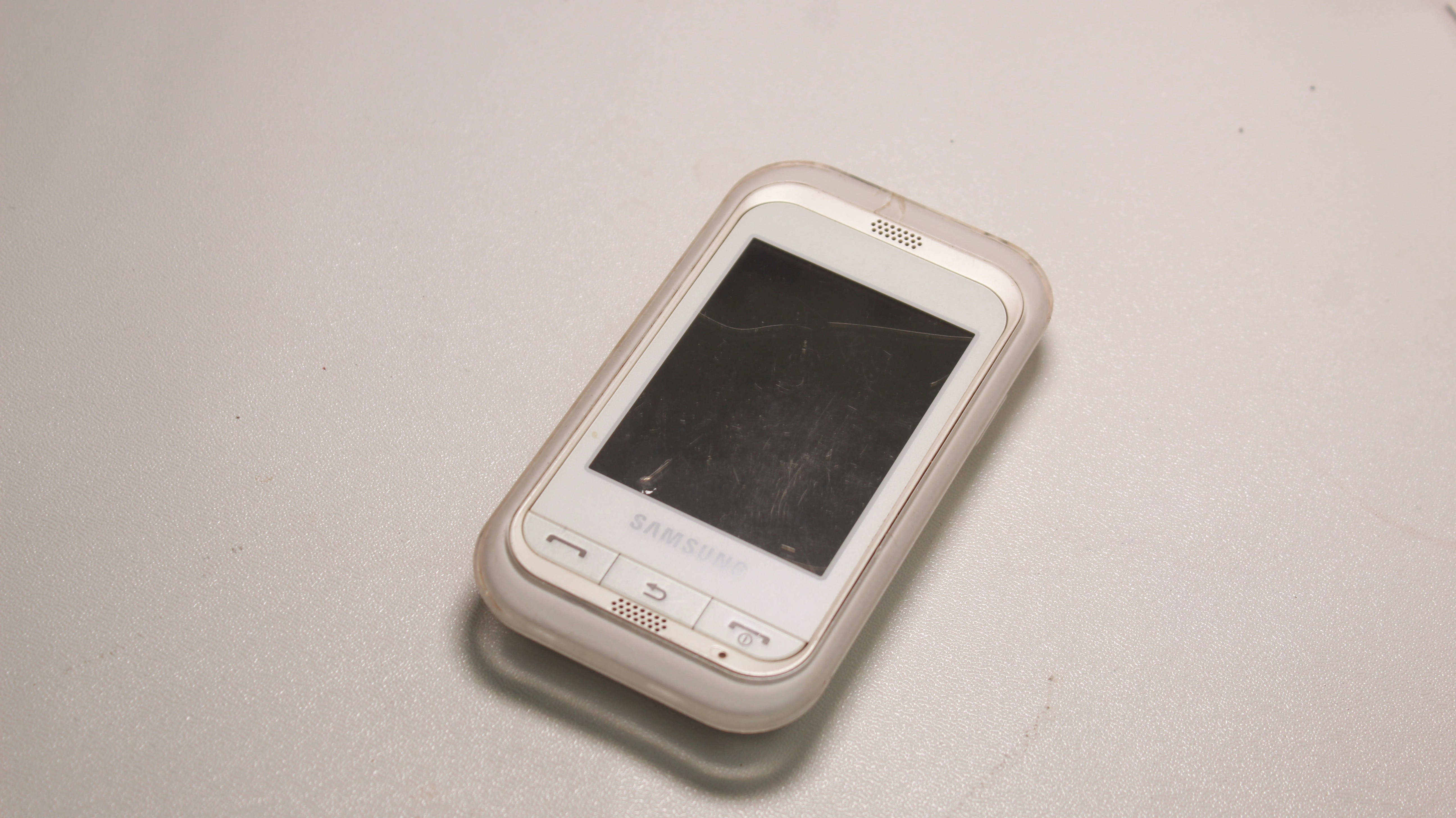 Samsung phone with shattered display, dark workshop, dim lighting