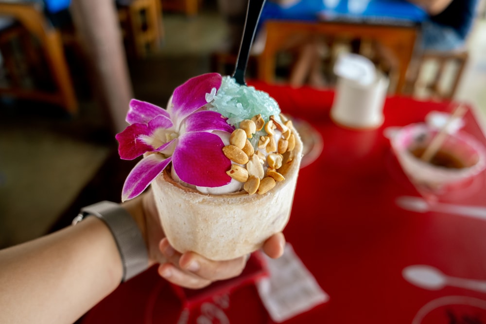 a person holding a cup of ice cream with a flower on top