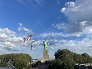 Close-up of hands signing immigration documents with the Statue of Liberty softly blurred in the background.