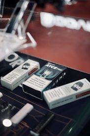 Several boxes of vaping products are displayed on a countertop. The boxes contain warnings about nicotine being a highly addictive substance. The setting appears to be a retail environment, possibly a vape shop.