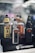 Several electronic vaping devices are displayed in a neatly organized manner. The devices have different color schemes including yellow and black, silver and black, orange and black, and all black. They are placed on a stand with a logo that reads 'Vaporesso'. The background is slightly out of focus with soft lighting and bokeh effects, giving a sleek and modern appearance.