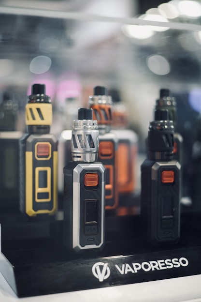 A vibrant collection of popular vape devices and flavors arranged on a wooden table under warm lighting.