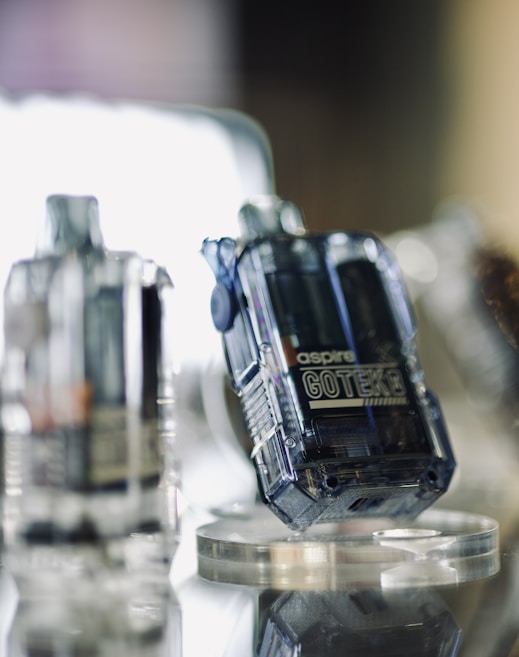 A close-up view of transparent electronic devices with a modern, sleek design placed on a mirrored surface. The focus is on a device labeled 'aspire GOTEK.' Other similar devices are blurred in the background, creating a futuristic and technological atmosphere.
