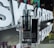 A transparent vaping device with the brand name 'aspire GOTEK X' is displayed prominently in front of illuminated letters spelling 'SK E-CRYSTAL'. The device is placed on a reflective surface, and the background includes various product boxes with colorful packaging.