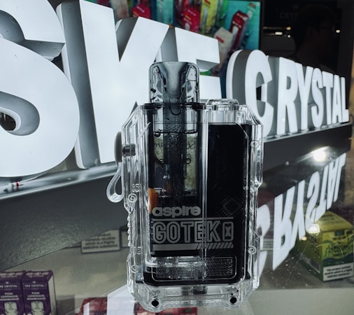 A transparent vaping device with the brand name 'aspire GOTEK X' is displayed prominently in front of illuminated letters spelling 'SK E-CRYSTAL'. The device is placed on a reflective surface, and the background includes various product boxes with colorful packaging.