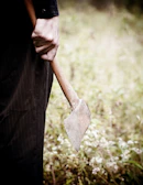 A hand holding a small hatchet with a leather-wrapped handle over fallen leaves.