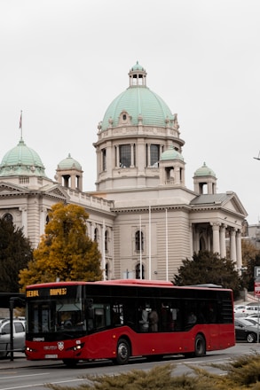 a red bus driving past a large white building