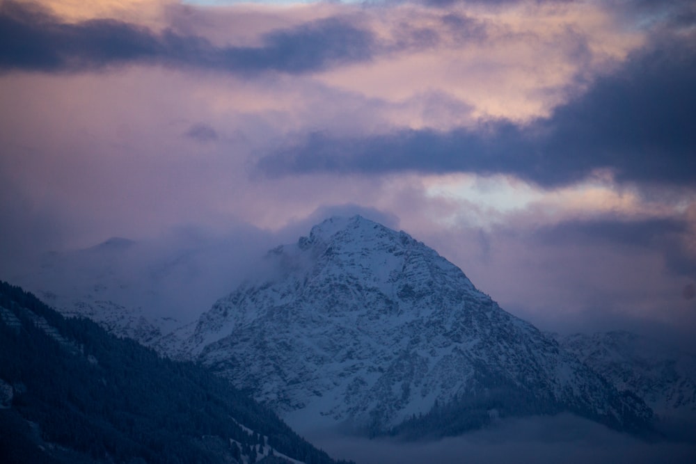 a mountain covered in snow under a cloudy sky