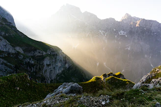 Sunlight filters through rugged peaks of the Prokletije mountains, casting golden hues over a winding hiking trail.