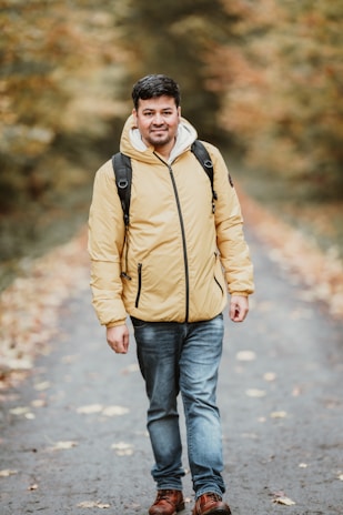 A candid shot of a person walking through autumn leaves, hoodie pulled up against the breeze.