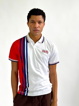 A person is wearing a sporty polo shirt featuring vertical red and blue stripes on a white background. The shirt has a design or logo with the number '1969' on the upper left side. The person's expression is calm and they are looking directly at the camera.