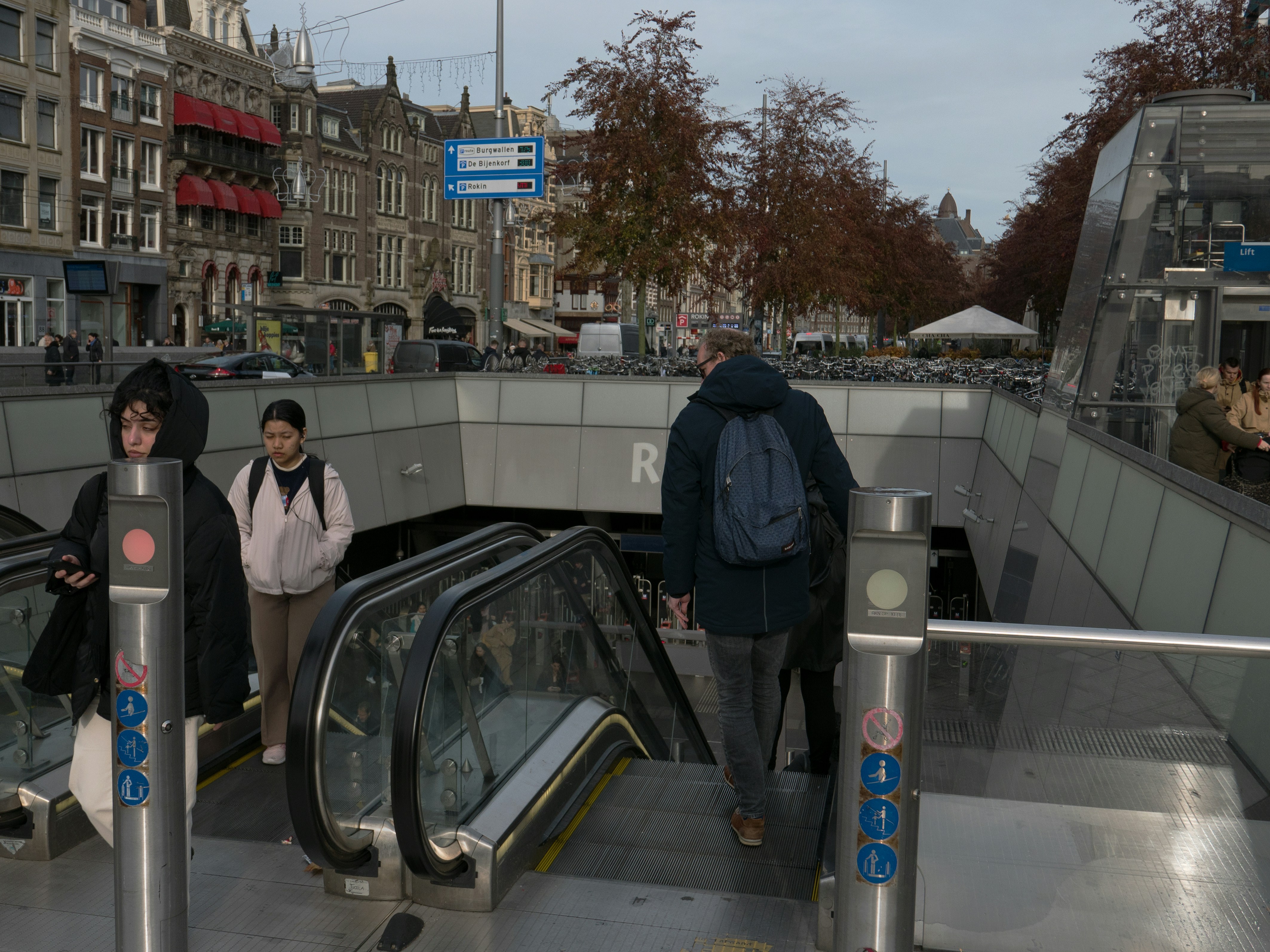 People are leaving or entering the metro station Rokin in Amsterdam downtown. This street is the Rokin in the city center, near Dam square. I like the modern architecture design of this subway stop. Street photography of urban transport in The Netherlands by Fons Heijnsbroek, 2023.