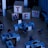 A dimly lit office space with several desks equipped with computers and office chairs. A mannequin-like figure is interacting with one of the desks. Large wooden blocks with the letters 'T', 'W', 'F', and a '?!' symbol are stacked in the background.