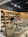 A cozy shop interior displays a variety of candles and accessories. Wooden shelves line the walls, filled with candles, vases, and decorative items. The central wooden table is adorned with an array of colorful dried flowers and various candle options. Large decorative jars and small potted plants add to the rustic aesthetic.