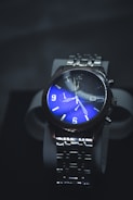 A luxurious wristwatch with a stainless steel strap and a striking blue dial. The watch face features illuminated numbers and hands, with additional dials for extra functionality.