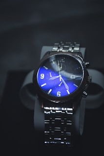 A luxurious wristwatch with a stainless steel strap and a striking blue dial. The watch face features illuminated numbers and hands, with additional dials for extra functionality.