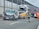 A collision involving a large truck, a van with significant front-end damage, and a street sweeper on a highway. Emergency responders, including firefighters and a person in orange, are present at the scene. The road is partially blocked, and debris is scattered across the pavement.