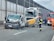 A collision involving a large truck, a van with significant front-end damage, and a street sweeper on a highway. Emergency responders, including firefighters and a person in orange, are present at the scene. The road is partially blocked, and debris is scattered across the pavement.