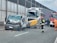 A collision involving a large truck, a van with significant front-end damage, and a street sweeper on a highway. Emergency responders, including firefighters and a person in orange, are present at the scene. The road is partially blocked, and debris is scattered across the pavement.