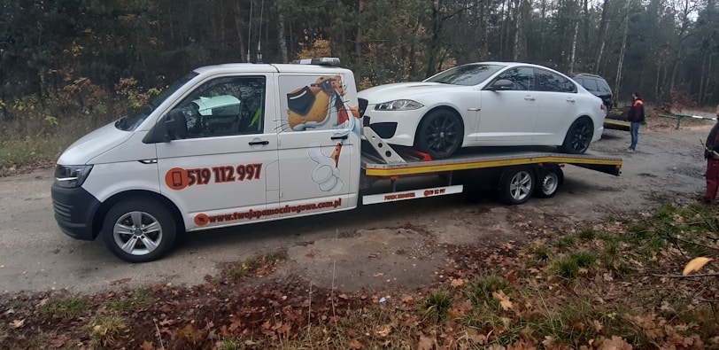 Tow truck lifting a stranded car on a dark highway illuminated by safety yellow lights.