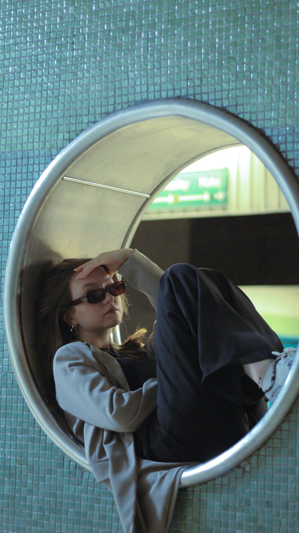 a woman sitting in a round mirror on a tiled wall