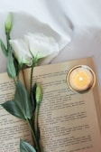 A softly glowing candle flickering beside an open book of Buddha Dhamma teachings.