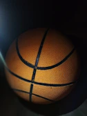 Close-up of a basketball spinning on a player's fingertip, glowing with fiery orange and gold hues.