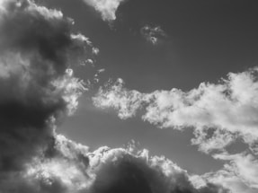 Dark stormy clouds fill the sky with patches of lighter, fluffier clouds creating an intense and dramatic contrast. The overall composition suggests movement and change, with shadows highlighting the texture of the clouds.