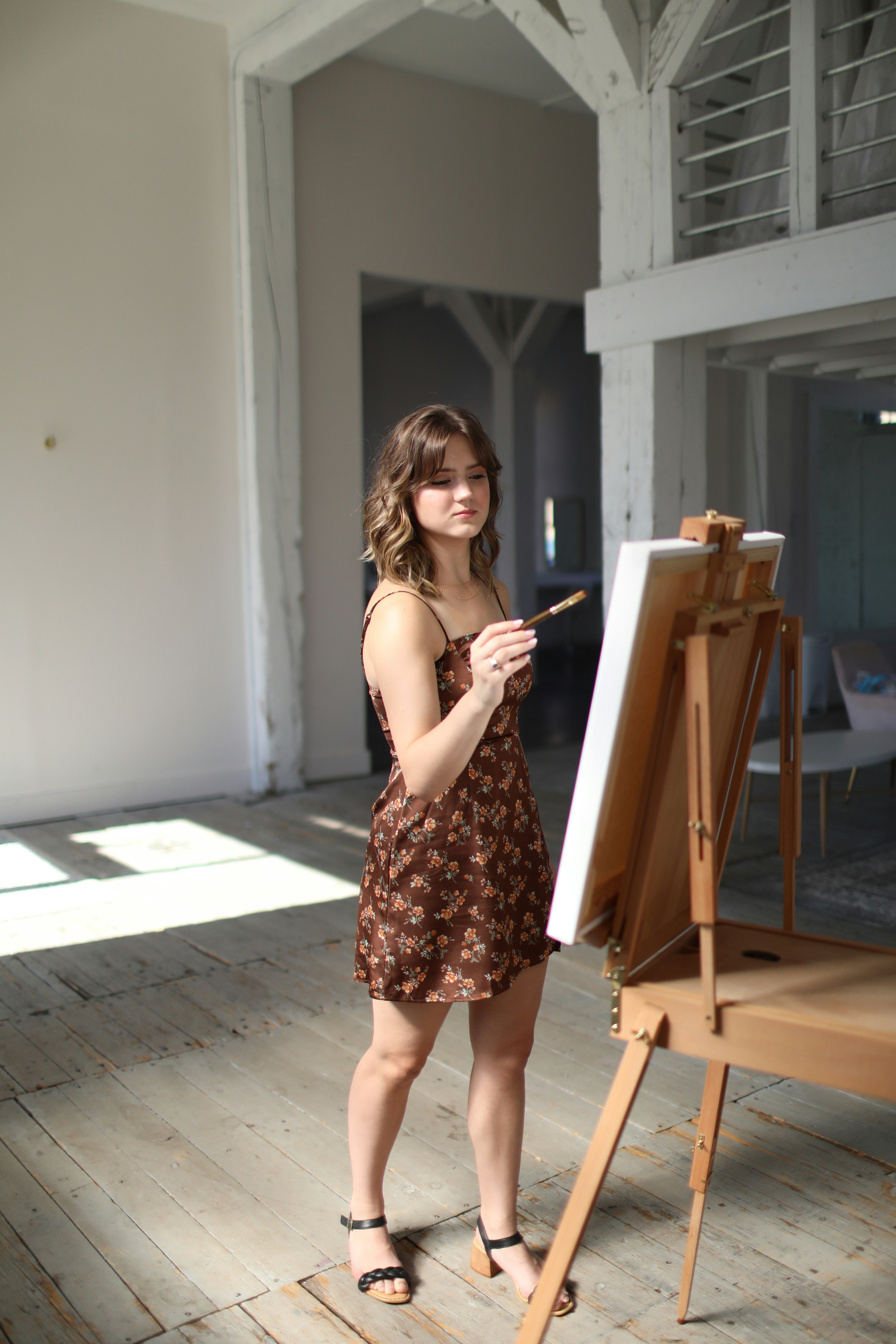 a woman standing in front of a easel holding a paintbrush