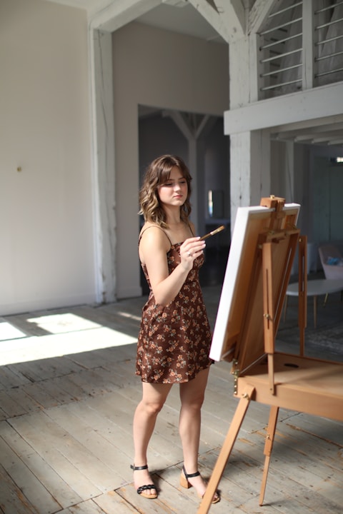 a woman standing in front of a easel holding a paintbrush